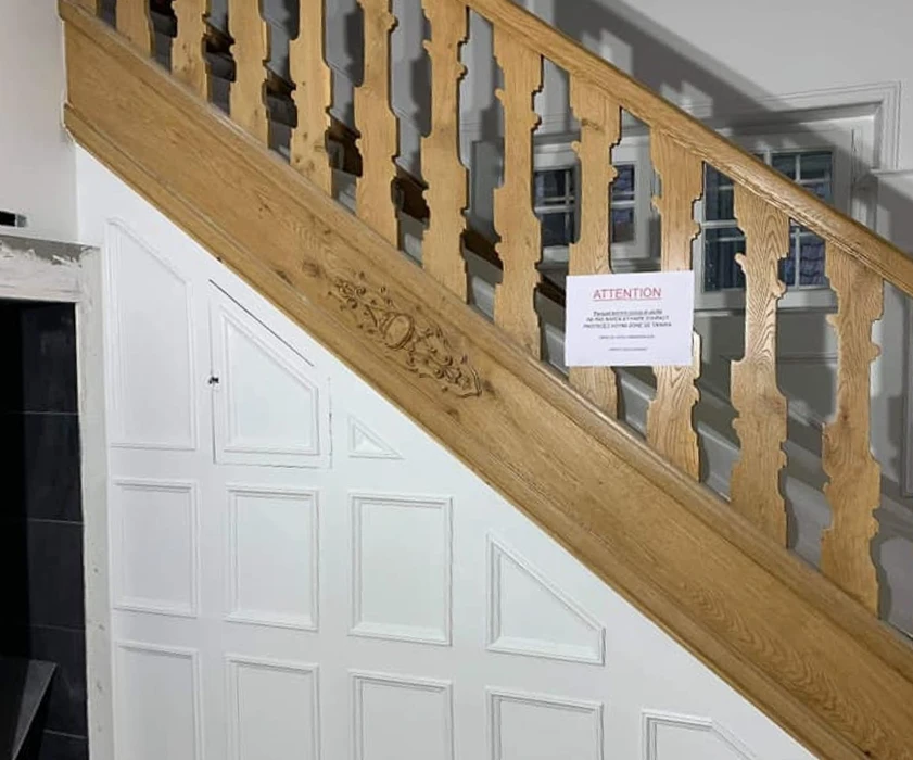 Escalier en bois avec rampe sculptée et balustres travaillés, panneau d'attention fixé sur la main courante