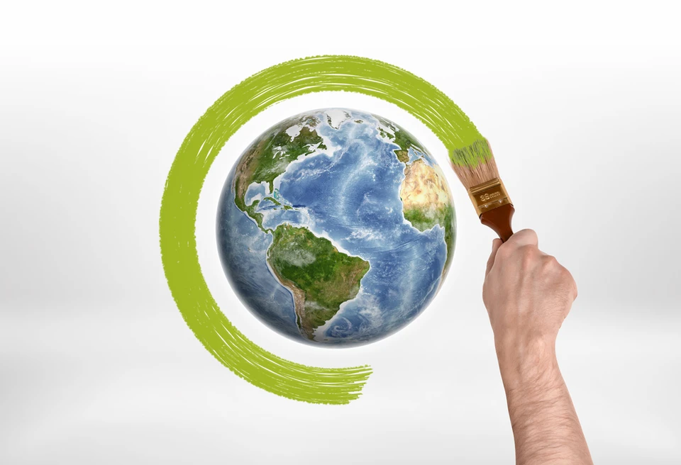 Une main tient un pinceau appliquant de la peinture verte autour d'une représentation de la Terre sur fond blanc