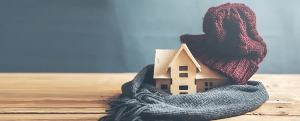Scène intérieure avec maquette de maison en bois posée sur table, enveloppée dans écharpes tricotées rouge et grise