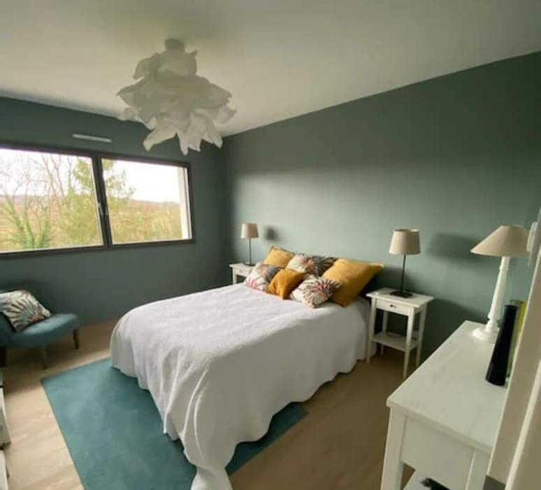 Chambre moderne avec murs verts, lit double à linge blanc et coussins orange
