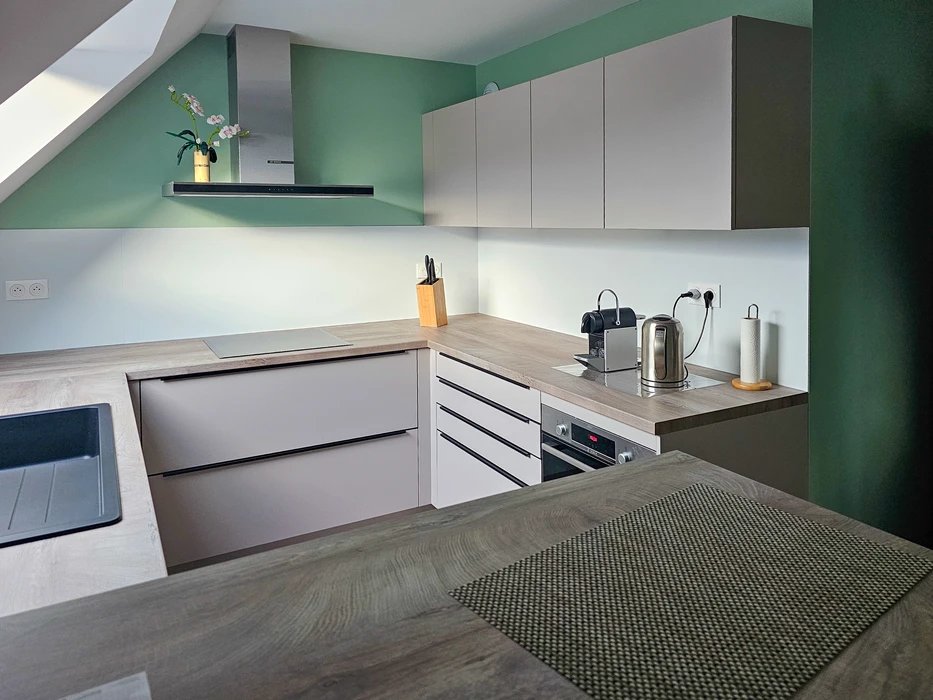 Cuisine moderne sous combles avec murs verts, mobilier blanc mat et plan de travail bois