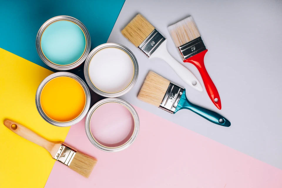 Scène d'atelier de peinture en intérieur avec pots de peinture ouverts et pinceaux disposés sur surface multicolore