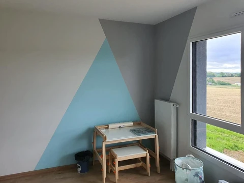 Chambre d'enfant en cours d'aménagement avec mur peint en motif géométrique triangulaire bleu et gris