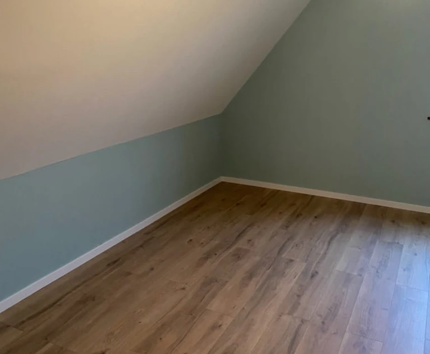 Pièce vide sous combles avec murs peints en vert sauge et plafond blanc mansardé