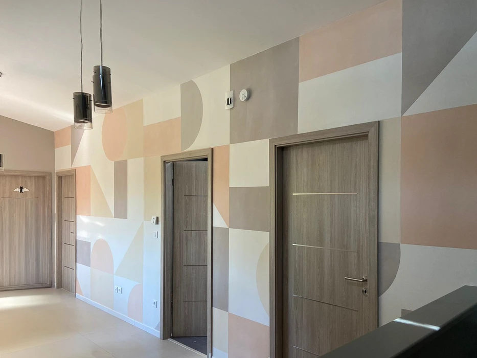 Mur peint décoratif représentant une architecture méditerranéenne stylisée avec arcs, escaliers et bâtiments en tons rosés et blancs